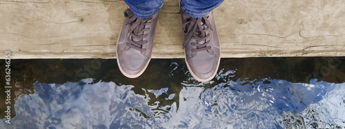 Banner with legs in brown moccasins on background mountain river. Feet of woman or man in brown shoes standing on wooden log above water. Concept of life balance, lifestyle. Header for website, blog