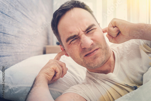 man at home tries to fall asleep, noisy neighbors interfere with sleep, an guy closes his ears with hands tired after work