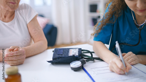 Physician checking old female patient blood pressure and writing down results