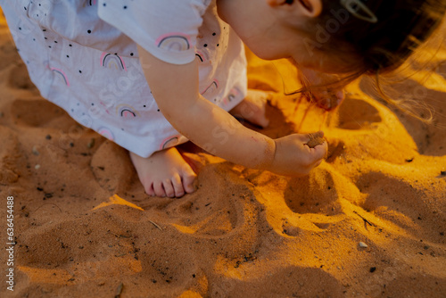 Small girl playing in beach sand during sunset in white dress with small rainbows
