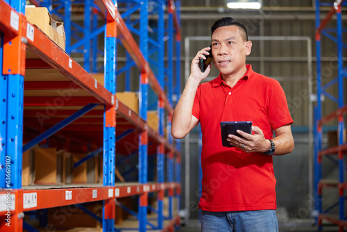 worker holding a tablet and talking on smartphone in the warehouse storage