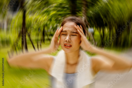 Asian woman exercising outdoors with discomfort hands gently massaging her head in too hot weather feeling sick dizzy fainting cerebral ischemia. Tired, supporting the body from slipping.