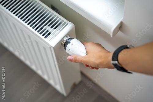 A woman's hand turns the battery heating knob. Heating in an apartment, at home. Heating prices.