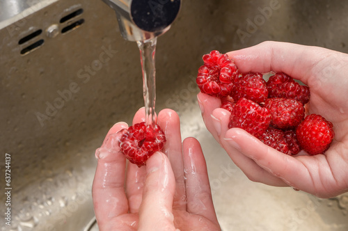 Dokładne mycie owoców pod strumieniem bieżącej wody, dojrzałe słodkie maliny 