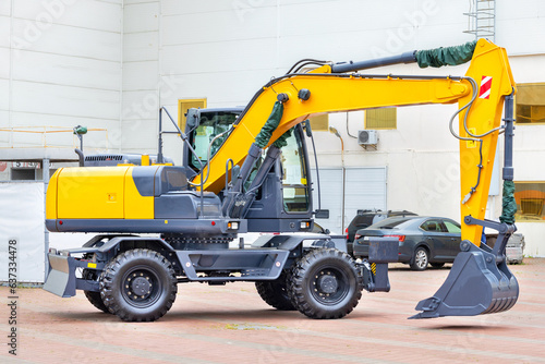 A wheeled construction excavator is parked in a paved car park on a bright day.