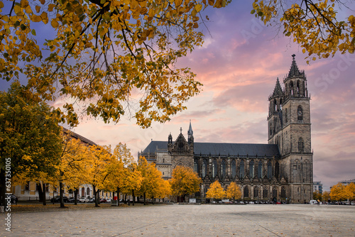 Scenic view of old ancient Magdeburger Dom cathedral at Dom square in Magdeburg old city center in bright orange autumn trees foliage in dramatic sunset sky. Germany tourism and travel destiantion