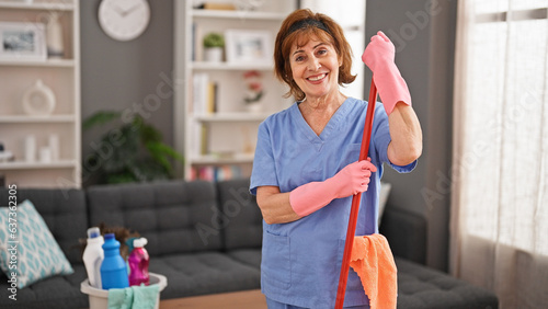 Middle age woman professional cleaner holding mop stick smiling home