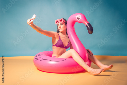 Funny summer photo shoot of beautiful brown hair model posing in studio wearing purple swimsuit and sun glasses barefoot. Studio light simulating sun in a photographyc studio of a charming woman