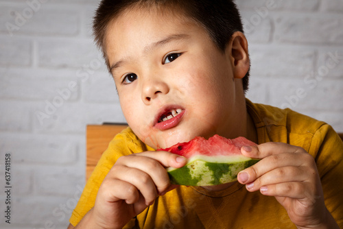 While enjoying the juiciest moments of summer. A boy without teeth enjoys a watermelon