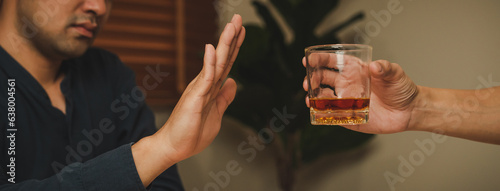 Alcoholism, sad depressed asian young man refuse, push alcoholic beverage glass, drink whiskey, sitting alone at night. Treatment of alcohol addiction, having suffer abuse problem alcoholism concept.