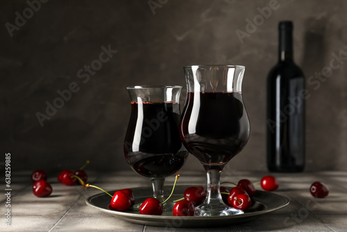 Glasses and bottle of sweet cherry liqueur with fresh berries on grey grunge table