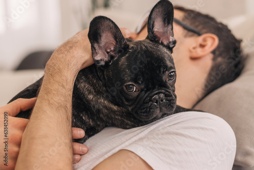 A young positive man is holding a puppy, a black French Bulldog, in an apartment.The concept of care, training,raising of animals.