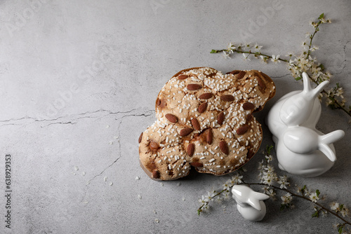 Delicious Italian Easter dove cake (Colomba di Pasqua), flowers and bunny figures on grey table, flat lay. Space for text