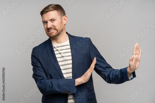 Frustrated man with disgust on serious face incredulously pushes away troubles with gesture of hands isolated on gray background. Male with angry expression refuse something bad showing denial.
