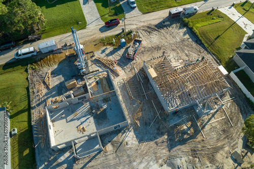 Professional builders and crane truck working on roof construction of unfinished suburban home with wooden frame structure in Florida rural area. Concept of housing development in America