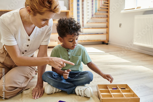 Montessori school, early school education, teacher pointing at wooden box near african american boy