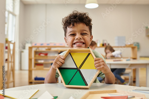 positive african american boy holding wooden didactic materials in blurred montessori school