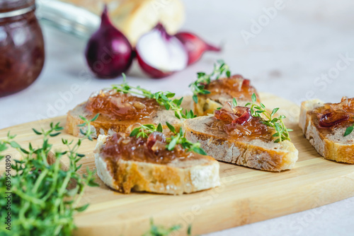 Homemade caramelized onion confit on a slices of bread with liver pate, fresh thyme, served on a wood serving board, selective focus. Healthy organic food