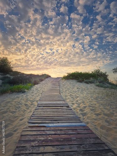 Wooden pathway through the sand leading to the beach and a beautiful morning sky with fluffy clouds