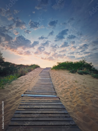 Wooden pathway through the sand leading to the beach. Beautiful morning sky with fluffy clouds