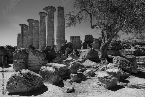 Black and white photography portraying the ruins of the temple of Heracles, doric columns and fallen rocks at the Valley of Temples in Agrigento, Sicily, Italy