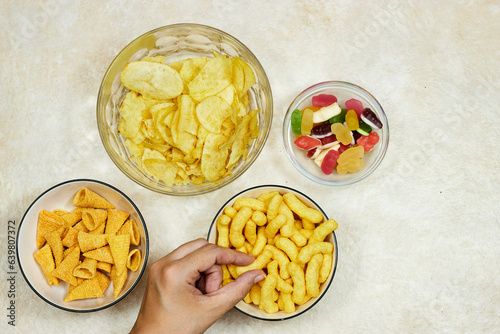 bowls of different chips and jelly candies on grunge background and hand holding one piece of chips