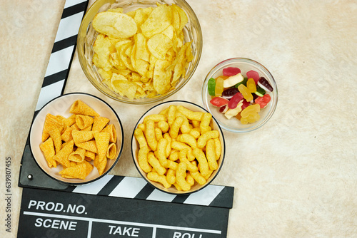 clapper board of video cinema in studio and bowls of different chips and jelly candies on grunge background