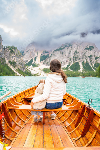 Woman with her daughter sitting in big brown boat at Lago di Braies lake in cloudy day, Italy.
