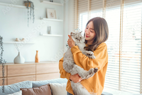 Happy young asian woman hugging cute grey persian cat on couch in living room at home, Adorable domestic pet concept.