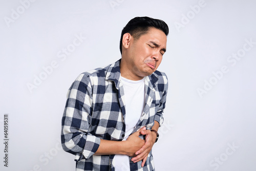 Abdominal Pain. Unhealthy young Asian man in casual shirt suffering from stomachache isolated on white background. Health problem concept