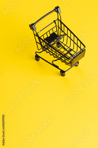 Vertical image of black shopping trolley with copy space on yellow background