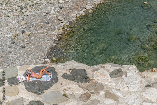 A woman sunbathes while reading a magazine lying on the rocks on the bank of the Trebbia river in Bobbio, Italy