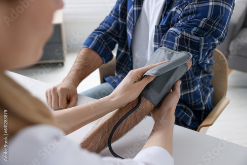 Doctor measuring blood pressure of man at table indoors, closeup