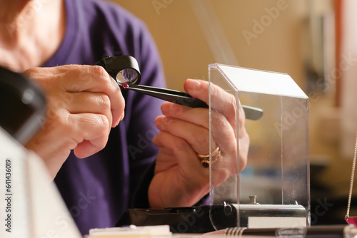 A gem specialist analizing a red ruby gemstone using tweezers and a loupe lense. Close up image of a gemologist evaluating a gemstone. concept of Gemstone identification.