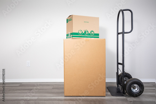 Cardboard moving boxes on hand truck indoors, ready for transportation.