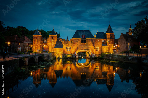 Medieval fortress city wall gate Koppelpoort and Eem River in the city of Amersfoort by night, Netherlands, Europe. Medieval town gate in Amersfoort, Netherlands.