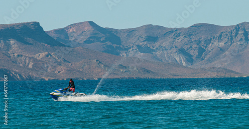 A guy on jet ski having fun in front of El Tecolote beach. In the background the isla Espiritu Santo on a sunny afternoon with blue sea and clear sky. La Paz Baja Mexico.