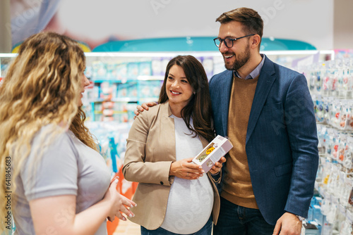 Attractive middle age couple enjoying in buying clothes and appliances for their new baby. Experienced saleswoman trying to help. Expecting baby concept.