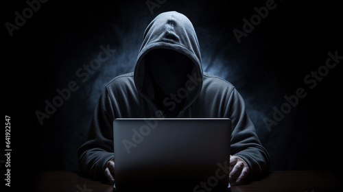 Person with Hidden Face and Laptop Engaged in Dark Cyber Work in a Black Background