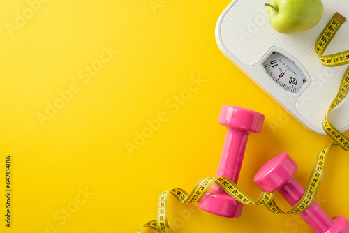 Fitness and Style Synergy. Overhead scene featuring weight scales, measuring tape, dumbbells, fresh green apple on bright yellow backdrop. Space for text or promotional material