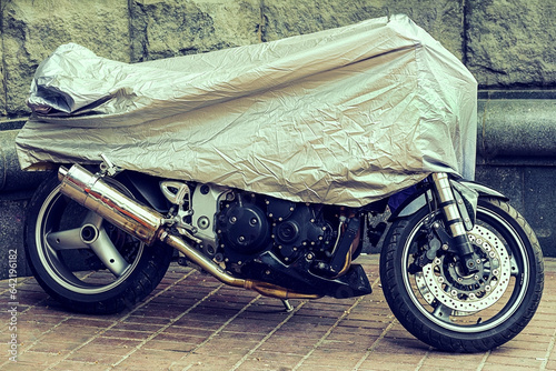 Covered Motorcycle. Parked motorcycle in a protective canvas, case. The motorbike covered with an oilcloth from a rain. Waterproof parking outdoors during travel.