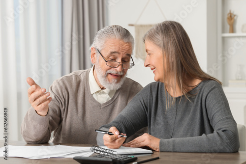 Elderly couple with papers discussing pension plan at wooden table indoors