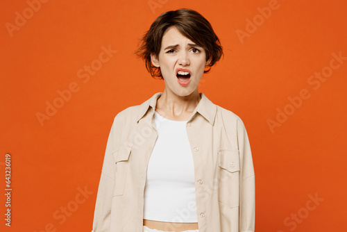 Young sad dissatisfied disappointed mad caucasian woman she wears beige shirt casual clothes look camera with opened mouth isolated on plain orange red background studio portrait. Lifestyle concept.