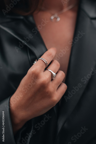 Close up fashion details of a black leather jacket and silver ring accessories. Fancy outfit, female accessories