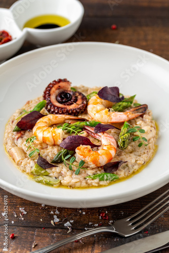 Risotto with jumbo shrimp and octopus on a white porcelain plate on wooden table. Seafood risotto