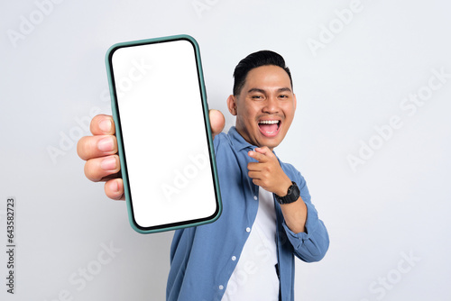 Excited young Asian man in casual shirt showing smartphone with blank screen isolated on white background