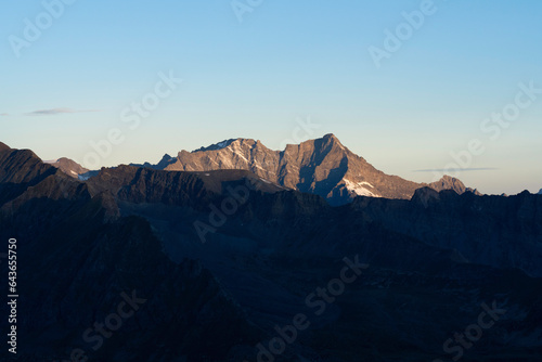 View of Grande Rousse, Rutor Massif from Gran Paradiso National Park glacier at sunrise. orange yellow colored peak in the background, foreground mountains and valley in the shadow