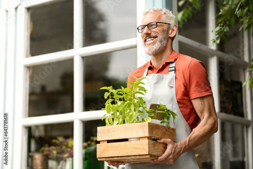 Handsome Mature Gardener Man Carrying Crate With Potted Plants Outdoors