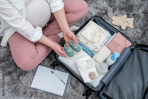 Pregnant woman's top view, floor-based preparations, packing with precision her maternity essentials, encapsulating the future mother's emotions