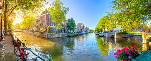 Soul of Amsterdam. Early morning in Amsterdam. Ancient houses, bridges, traditional bicycles, canals, boats, and the sun shines through the trees. Panoramic view with all the sights of Amsterdam.